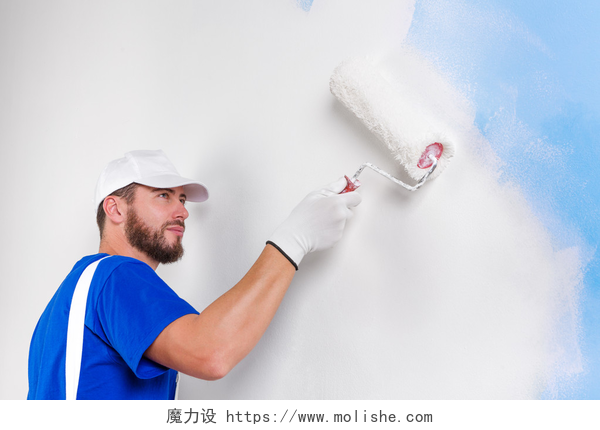 装修工人拿着刷子正在粉刷墙壁画家在白色工装裤，蓝色 t 恤